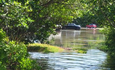 Sunny day a shallow pool of water covers a parking lot with two cars in the background